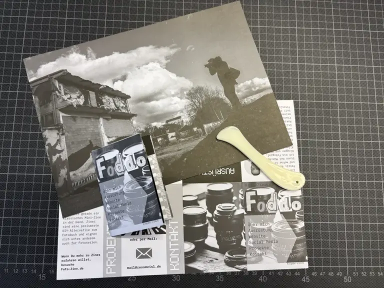 Schwarz-Weiß-Fotodrucke, Flugblätter und ein Papierschneider auf einer gerasterten Schneidematte.