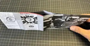 Eine Hand hält ein kleines, gefaltetes Schwarz-Weiß-Zine auf einer gitterartigen Oberfläche.